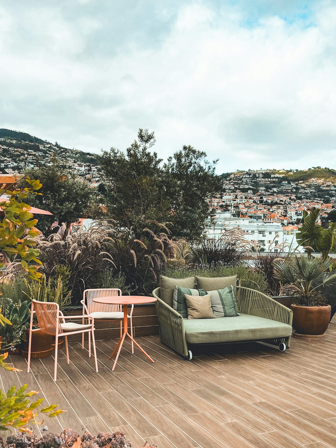 Bunte Terrassenmöbel stehen auf einer Veranda mit Blick auf eine hügelige Stadt.
